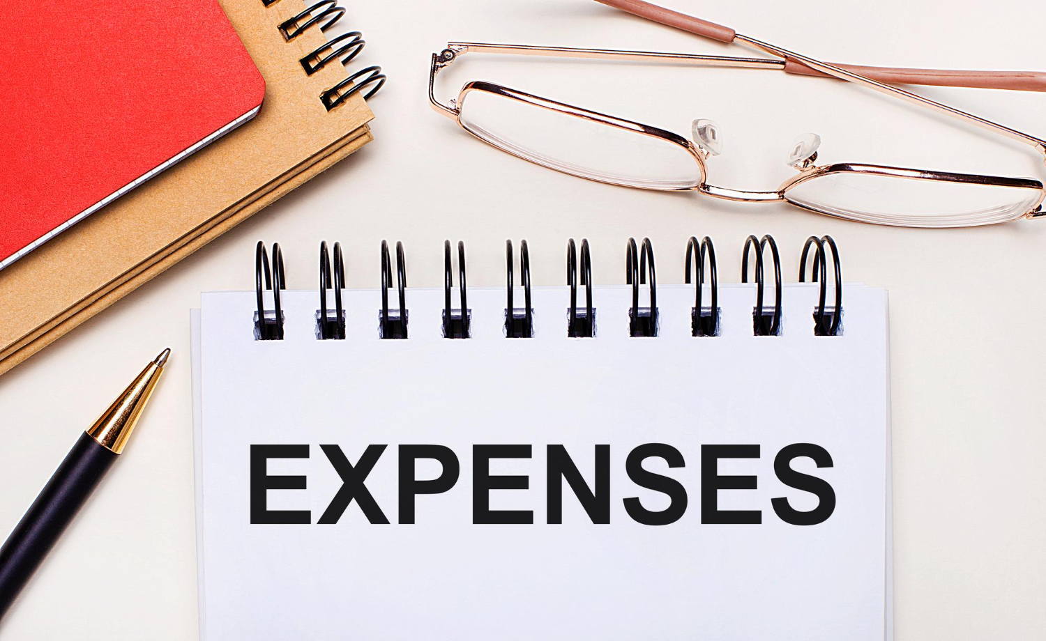 light-background-glasses-gold-frames-pen-brown-red-notepads-white-notebook-with-text-expenses-business-concept